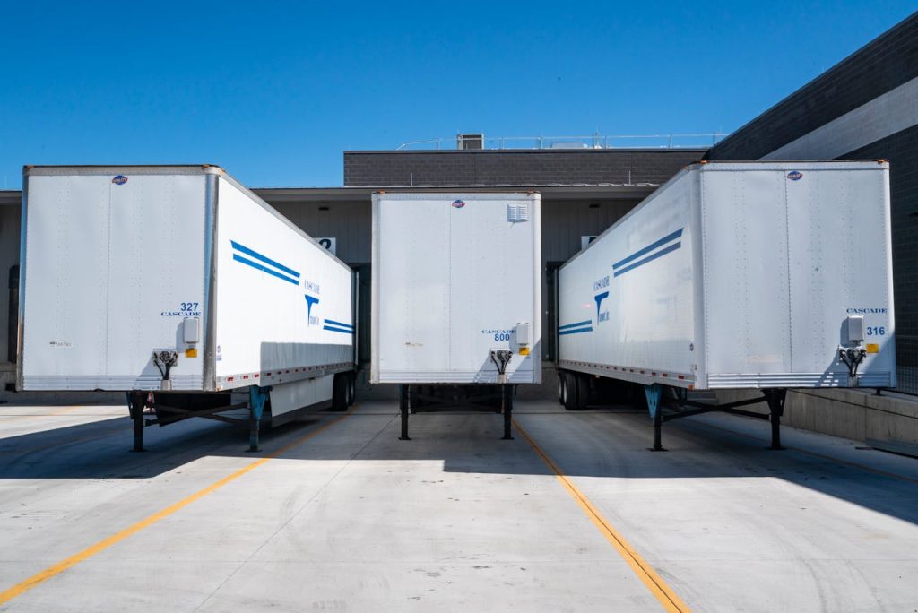 pexels photo 1267325 Three white cargo trailers parked at an industrial shipping dock under clear blue skies.